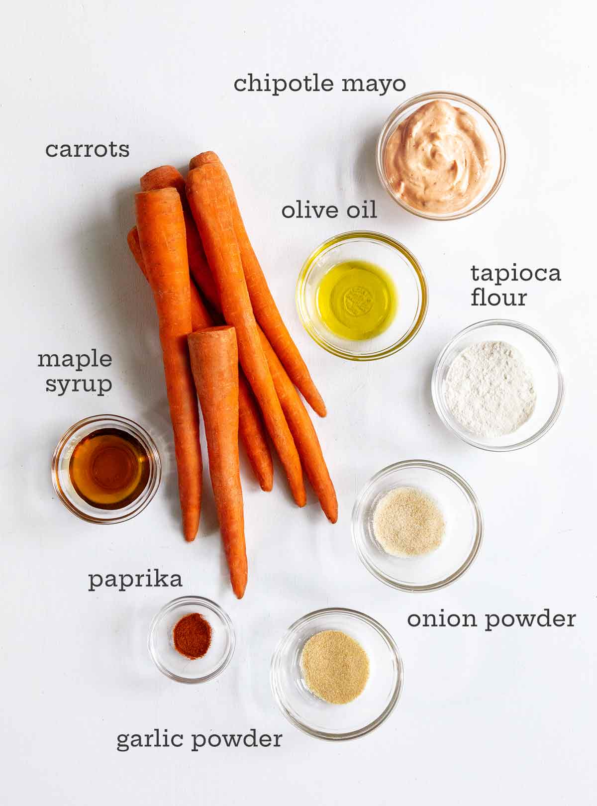 Carrots, mayo, oil, onion powder, garlic powder, maple syrup, and paprika on a white background.