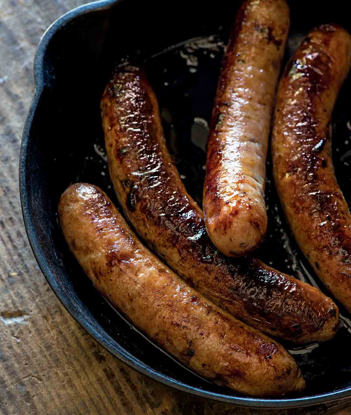 A cast-iron skillet with four cooked chicken apple sausages inside.