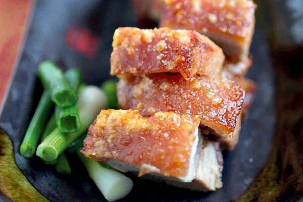 Pieces of Chinese roast pork in a black dish with chopped scallions beside it.
