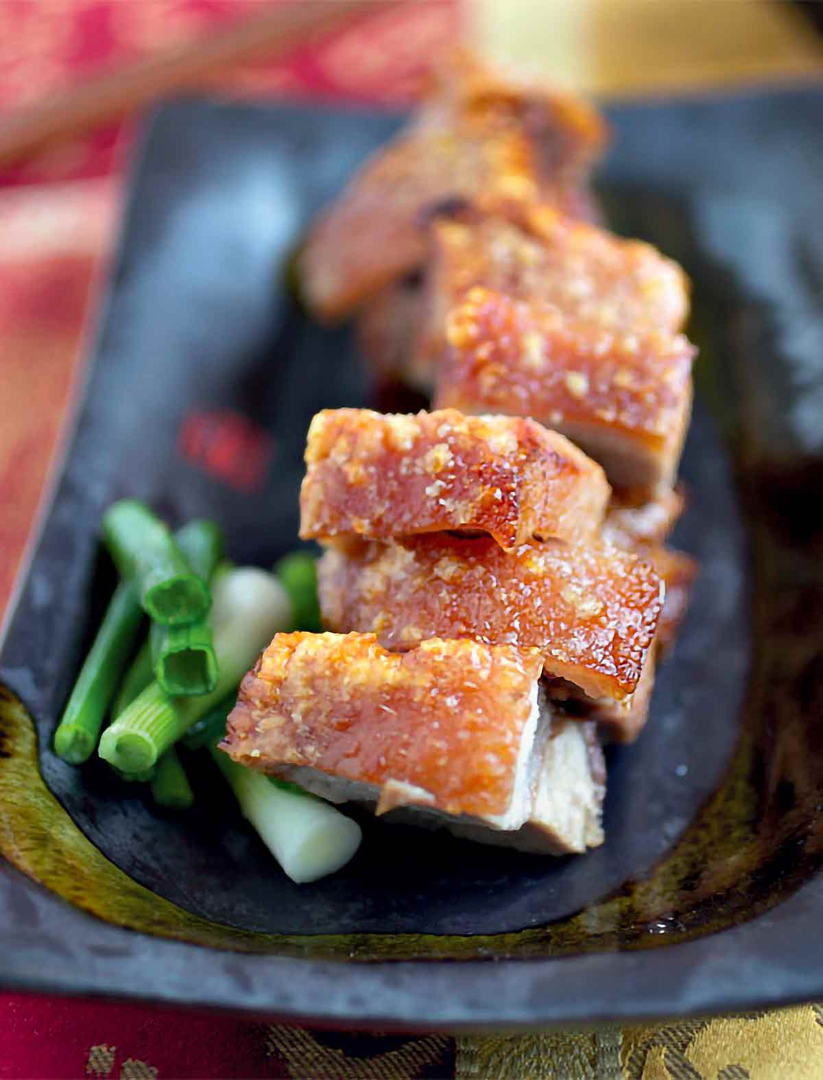 قطع من لحم الخنزير المشوي الصيني في طبق أسود بجانبه بصل أخضر مفروم.