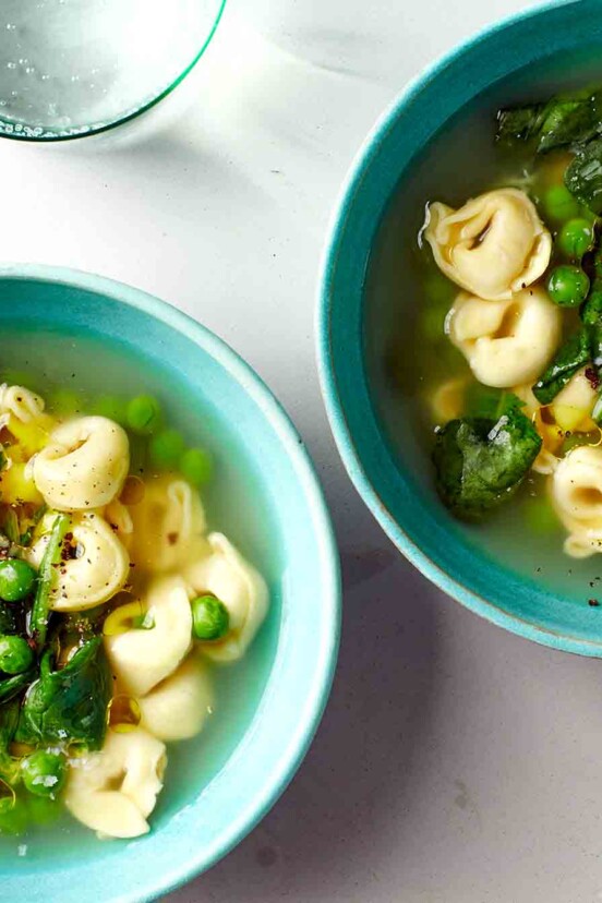 Two bowls filled with tortellini, peas, and spinach.