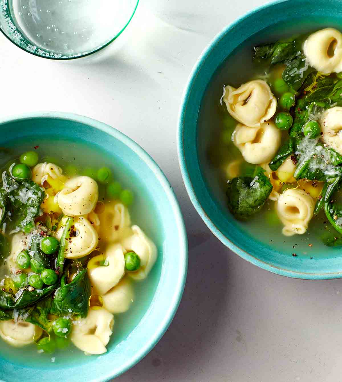 Two bowls filled with tortellini, peas, and spinach.