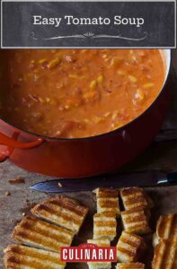A large pot of Ina Garten's easy tomato soup with a grilled cheese sandwich being cut into croutons beside it.
