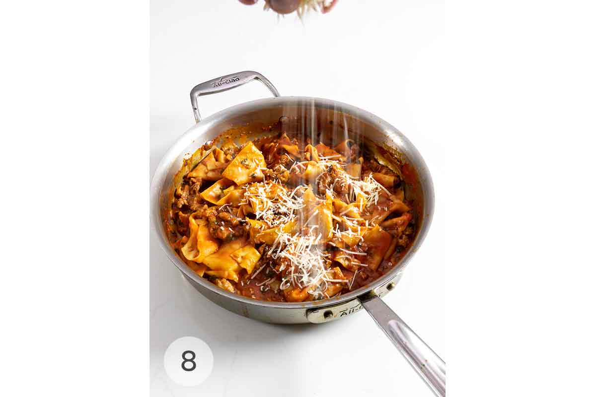 Parmesan cheese being sprinkled over a skillet of sausage pappardelle.