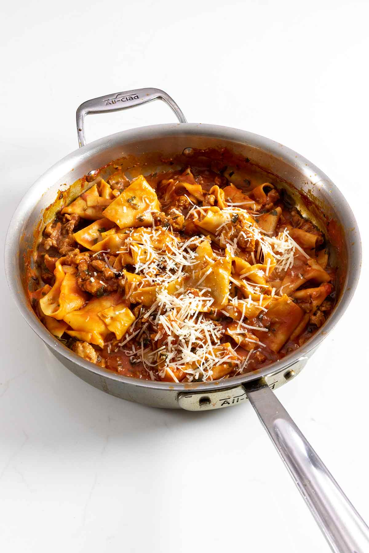 A skillet full of sausage pappardelle, topped with grated Parmesan cheese.