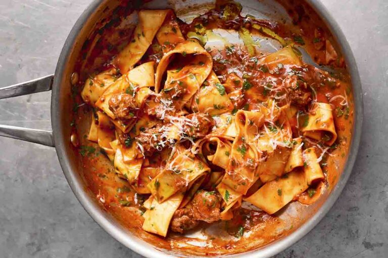 A metal skillet filled with sausage pappardelle with grated Parmesan on top.