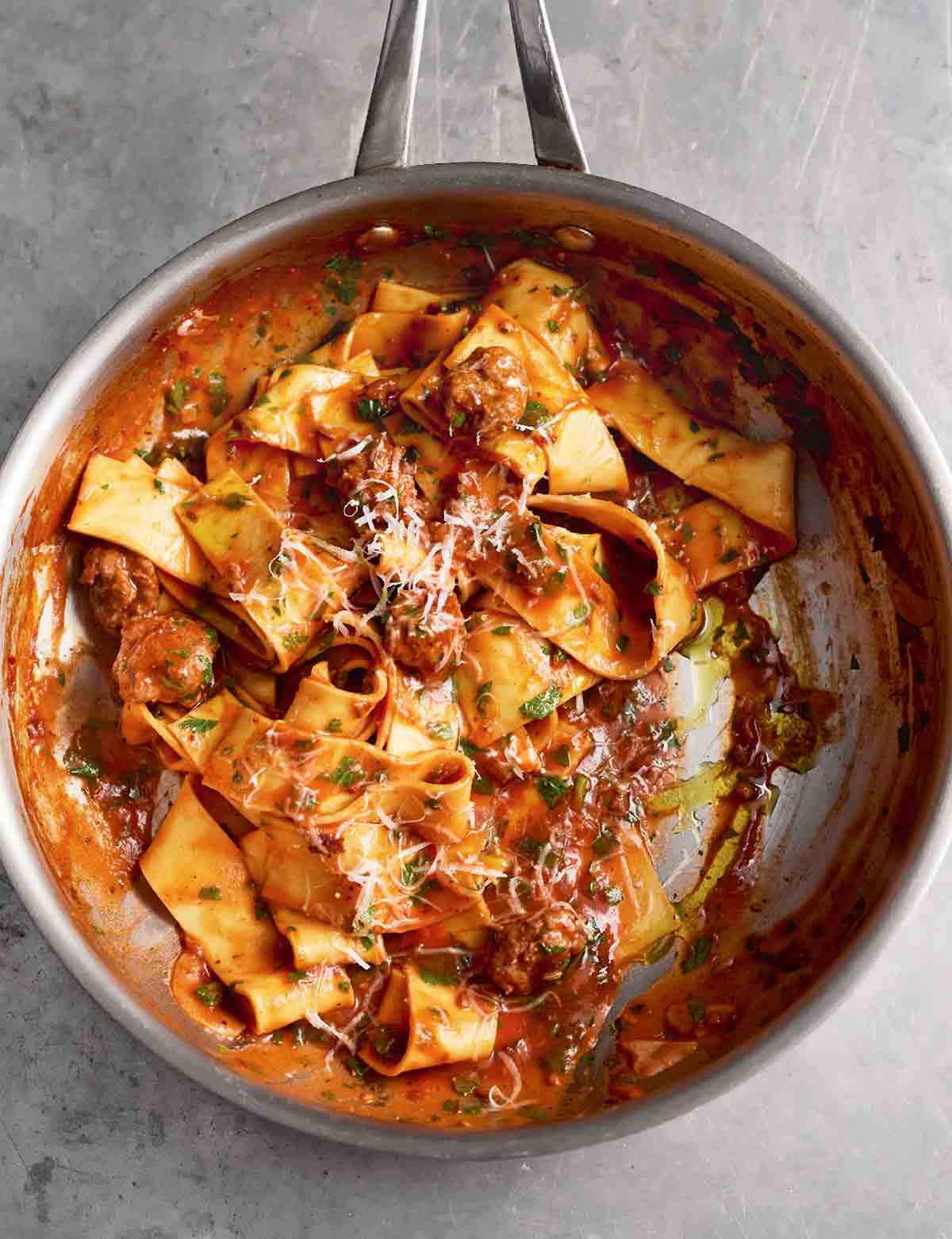 A metal skillet filled with sausage pappardelle with grated Parmesan on top.