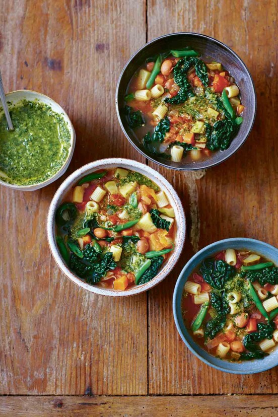 Three bowls of minestrone soup with a small bowl of pesto on the side.