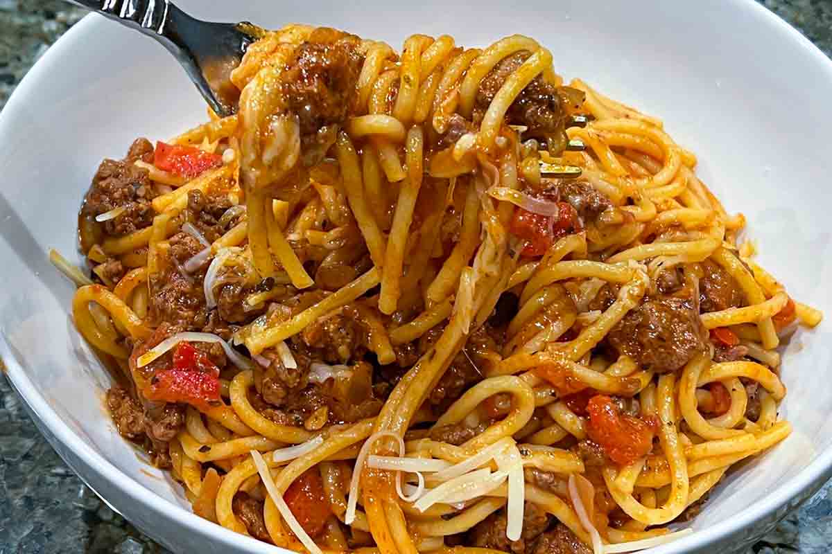 A white bowl filled with spaghetti and meat sauce with a fork scooping out a bite.