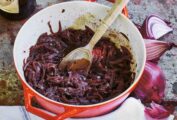 A red Le Creuset pot filled with red wine onions, that have been slowly cooked together.