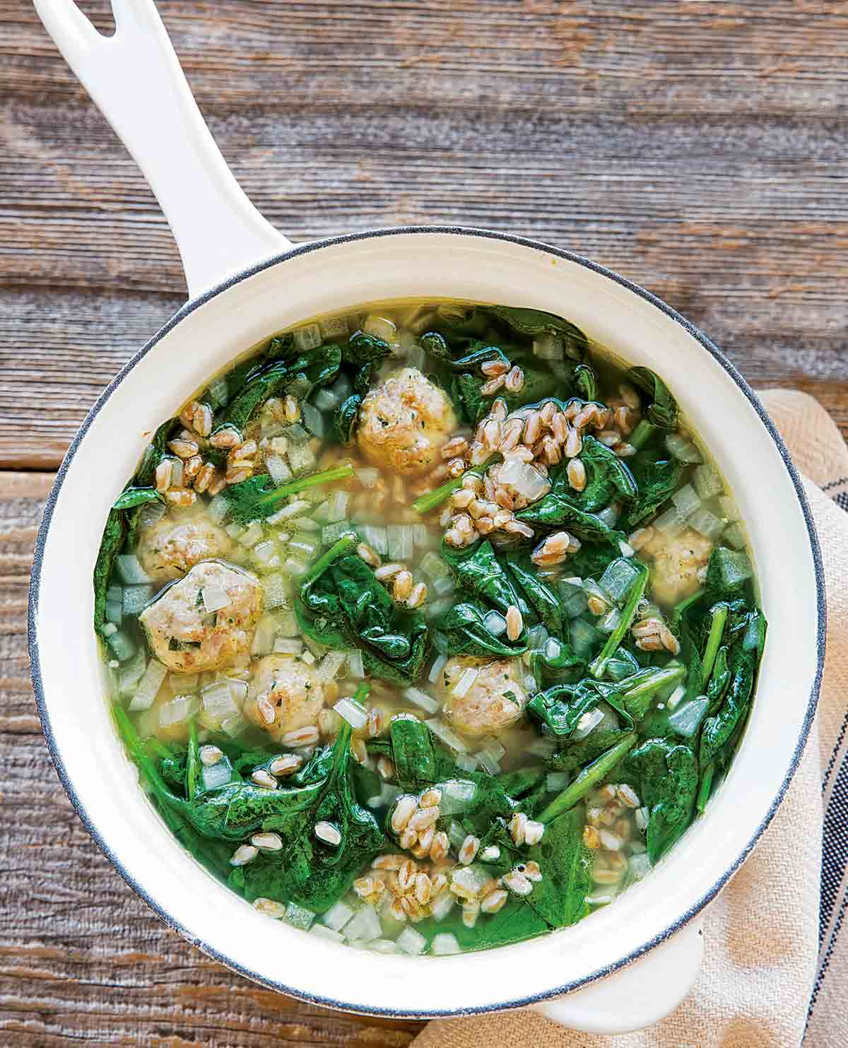 A white enamel pot filled with turkey meatball soup.