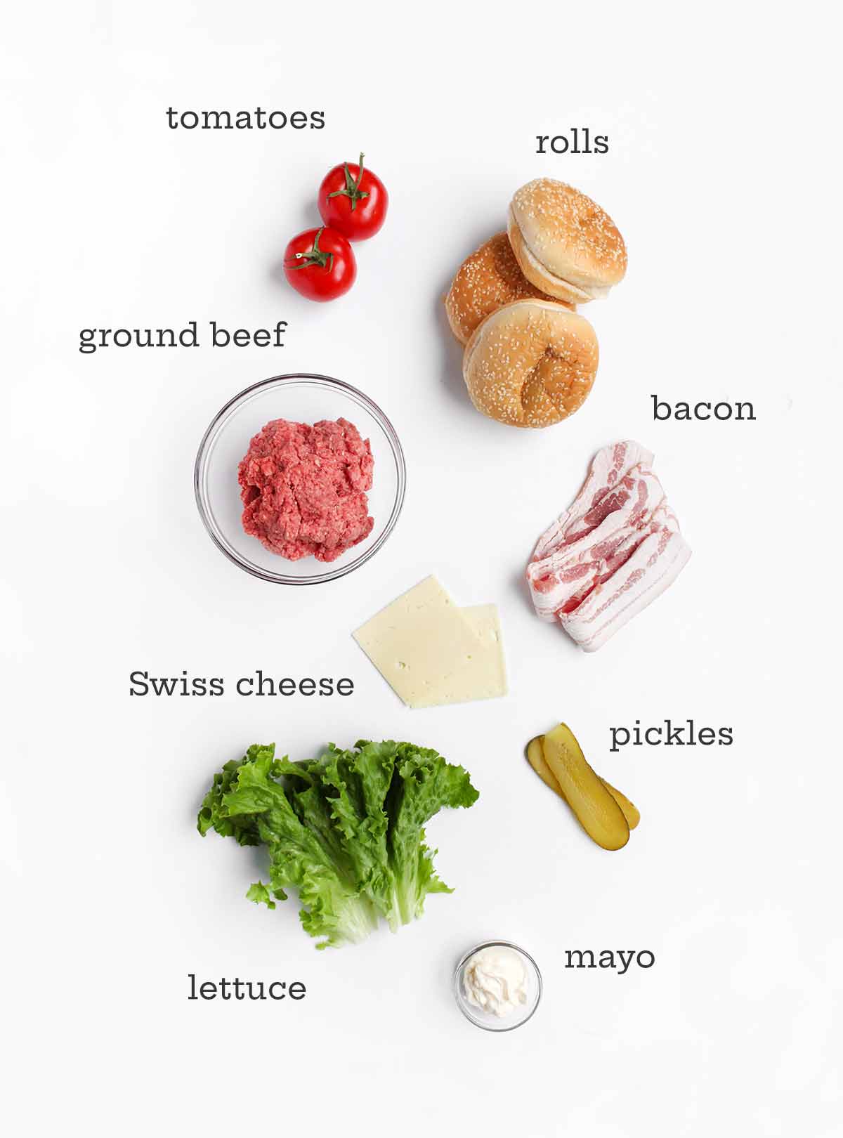 Ingredients for a bacon Swiss burger--beef, rolls, cheese, bacon, tomatoes, pickles, lettuce, and mayo.