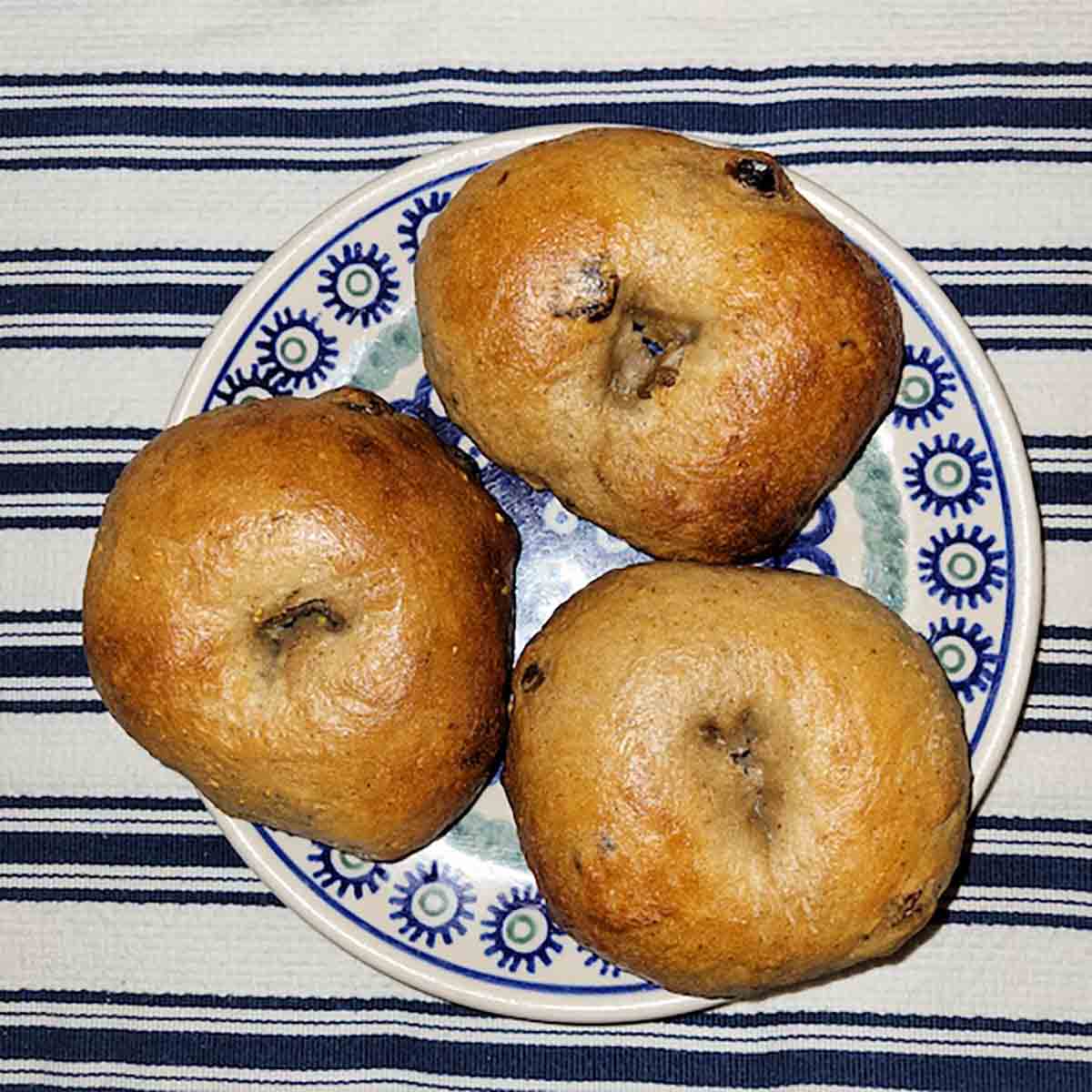 Three homemade cinnamon raisin bagels on a blue and white plate.