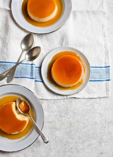 Three plates, each with a crème caramel on them with spoons resting on the side.