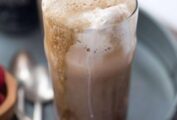 Two Guiness floats with straws on a grey metal try with a few spoons lying beside them.