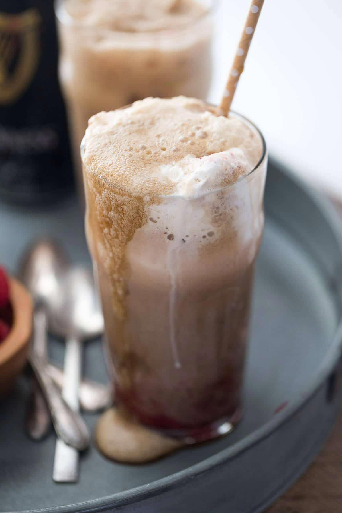 Two Guinness floats with straws on a gray metal container, with a couple of spoons next to them.