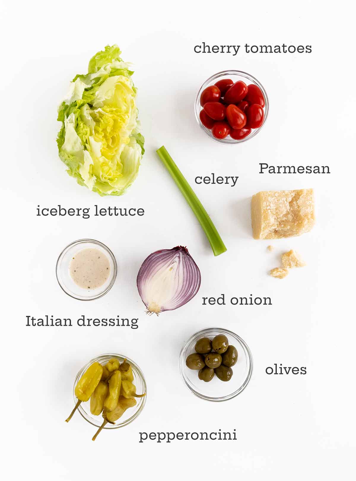 Ingredienser för italiensk sallad - sallad, tomater, selleri, parmesan, dressing, lök, oliver och pepperoncini.