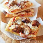 Three square slices of meatball pizza on strips of parchment paper, with fresh Parmesan sprinkled overtop.