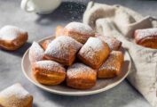 A pile of beignets dusted with confectioners' sugar in a bowl.