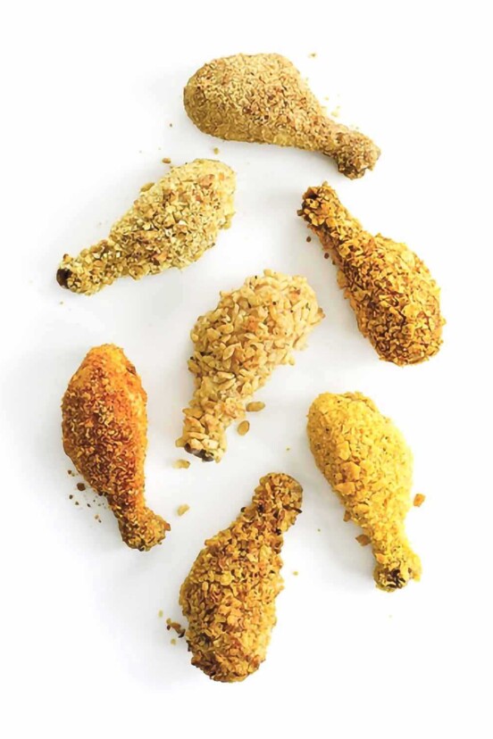 Seven oven fried drumsticks with different coatings on a white background.