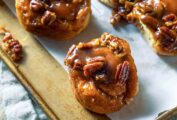 A rimmed parchment-lined baking sheet filled with quick sticky biscuits that are coated in thick syrup and topped with pecans.