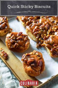 A rimmed parchment-lined baking sheet filled with quick sticky biscuits that are coated in thick syrup and topped with pecans.