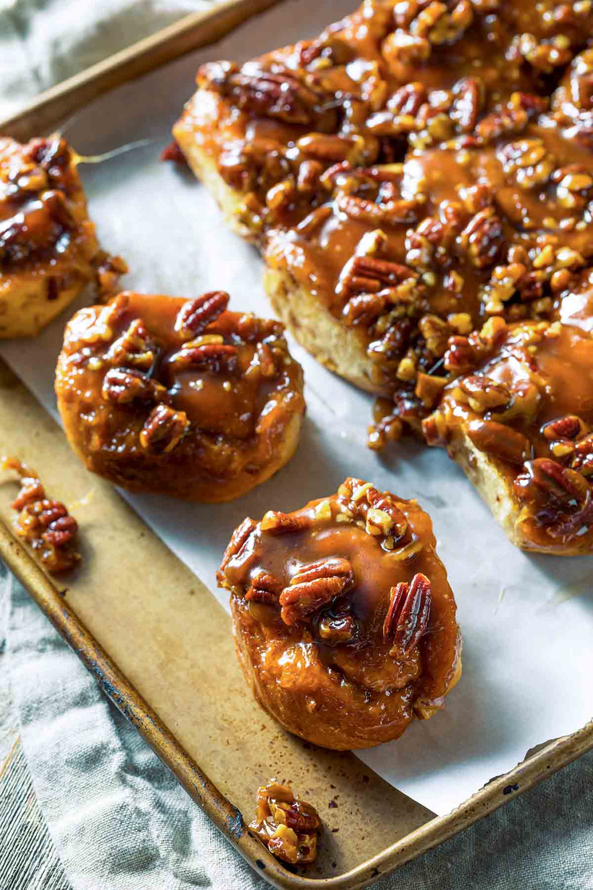 A parchment-lined rimmed baking sheet filled with quick-stick cookies, coated in thick syrup and topped with pecans.