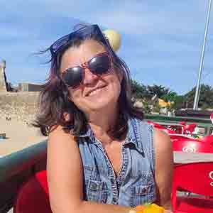 A woman with sunglasses at the beach smiling.