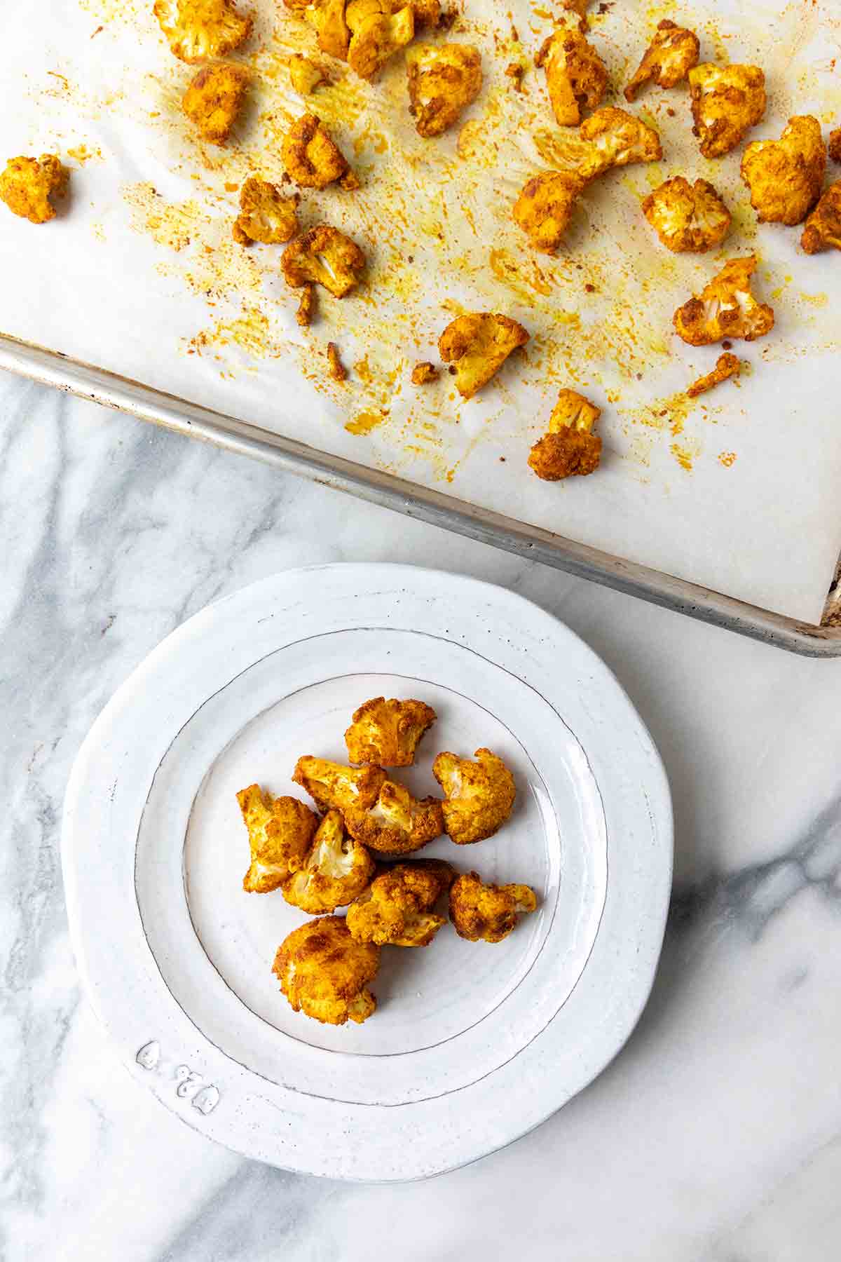 Florets of spicy roasted cauliflower on a white plate and on a baking sheet beside it.