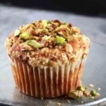 A single apple spice muffin with streusel and pistachios on an inverted metal cake tin.