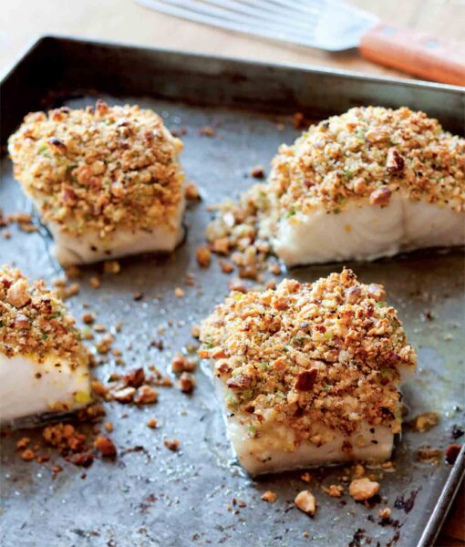 Four fillets of baked fish with almonds, lemon, and bread crumbs on a rimmed baking sheet.
