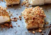 Four fillets of baked fish with almonds, lemon, and bread crumbs on a rimmed baking sheet.