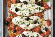Fish fillets on a sheet pan with roasted tomatoes and black olives.