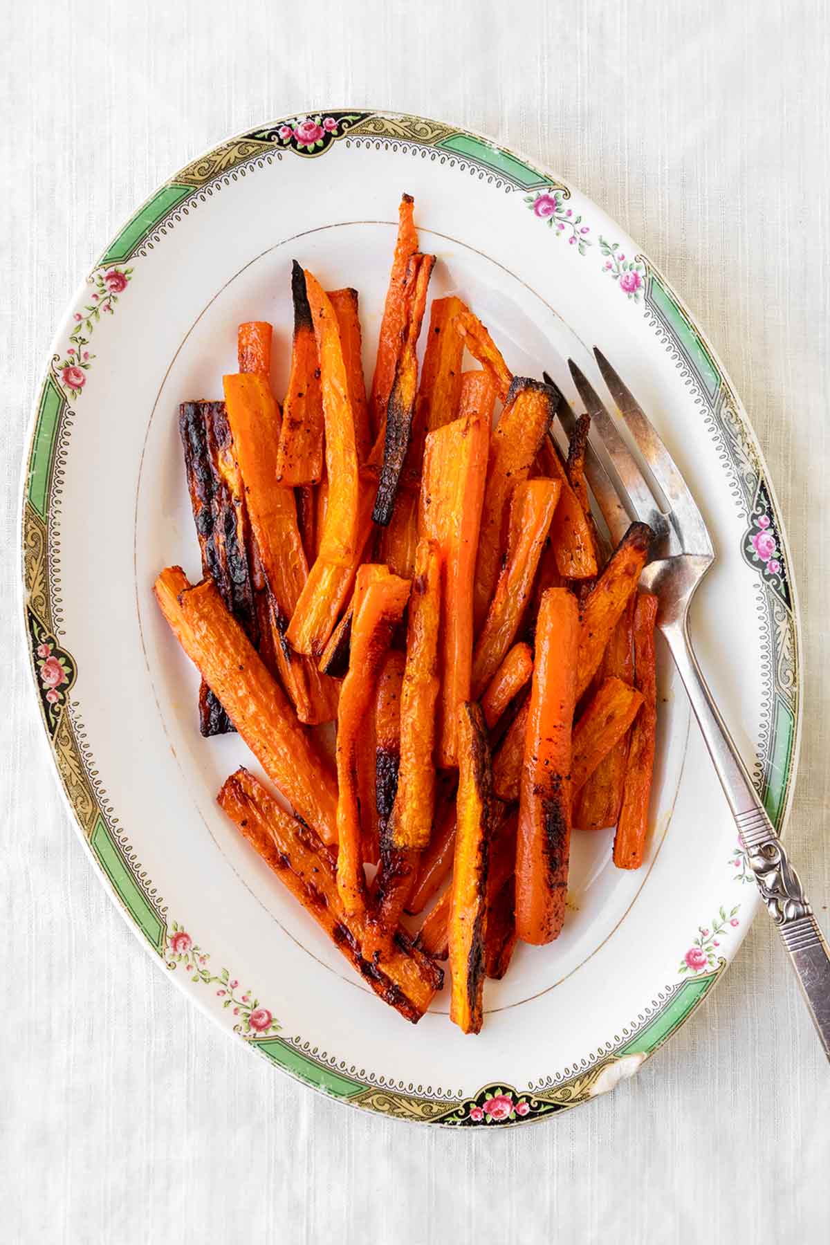 An oval platter filled with roasted carrots and a silver serving fork on the side.
