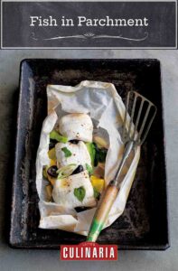 A rimmed baking sheet with fish in parchment and a fish spatula resting beside it.