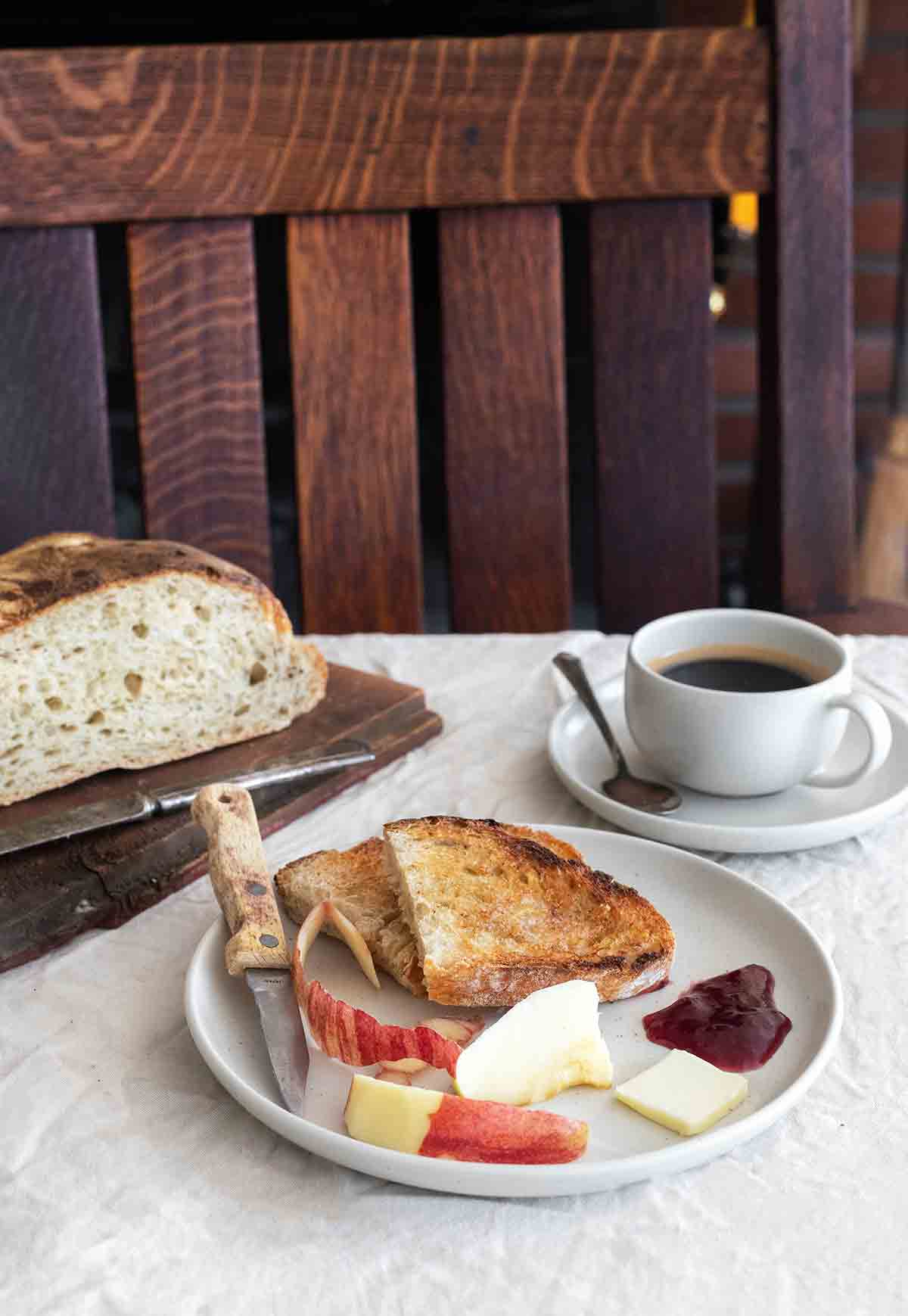 Two slices of toasted bread on a plate with a cut apple, a knife with butter, and a dollop of jam.