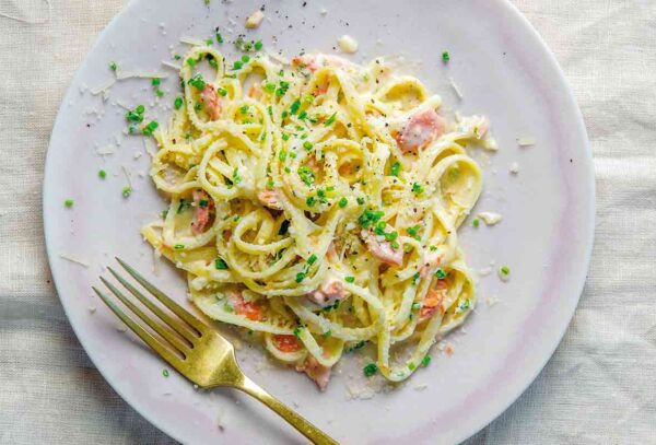 A white plate topped with a pile of lemony salmon pasta, sprinkled with chives.