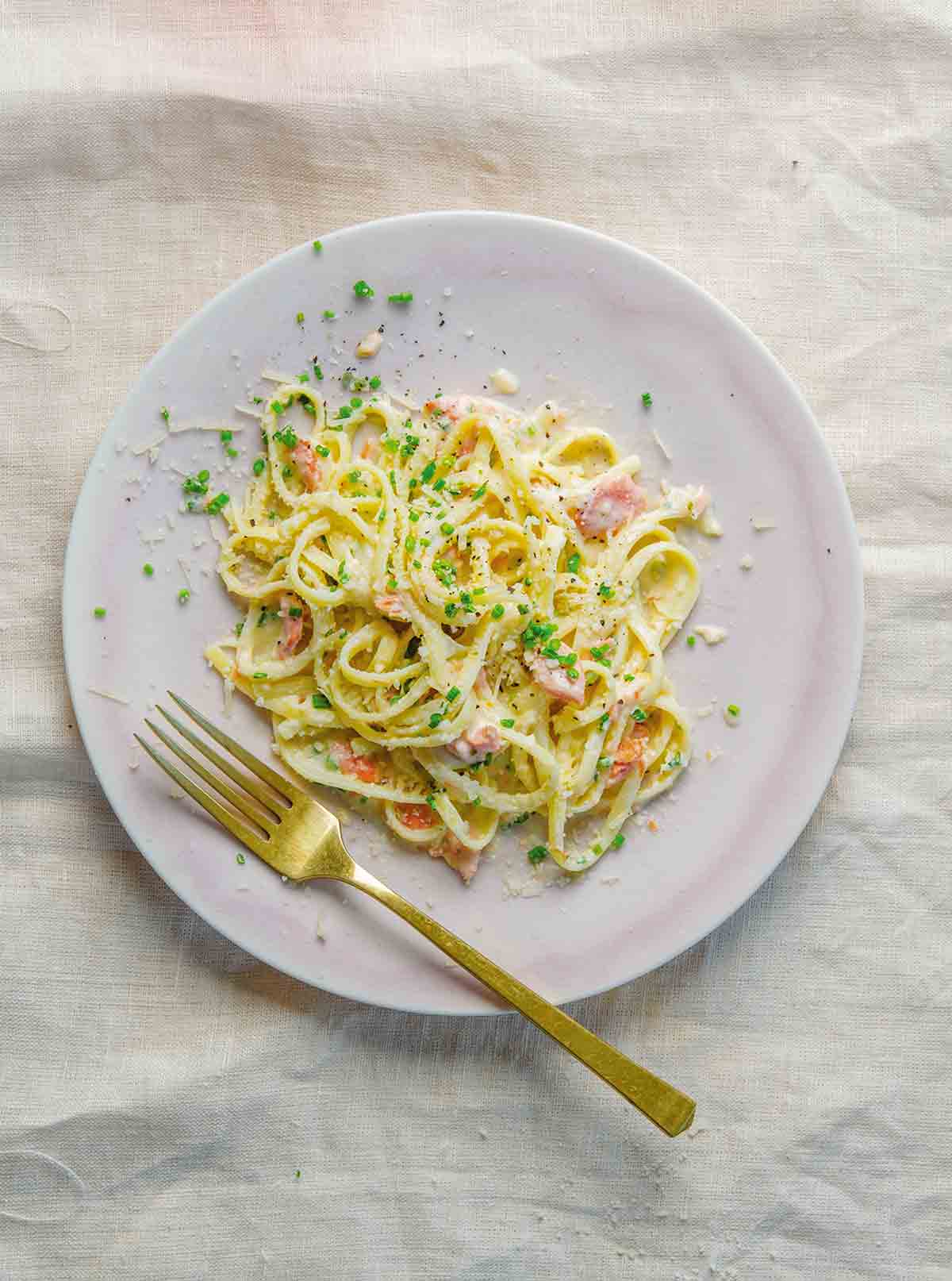 A white plate topped with a pile of lemony salmon pasta, sprinkled with chives.