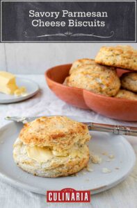 A savory Parmesan cheese biscuit with butter on a plate and a bowl of biscuits in the background.