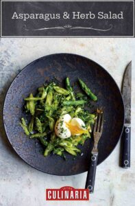 Asparagus and herb salad with chopped parsley, basil, tarragon, and mint and a broken soft boiled egg on a plate, fork and knife.