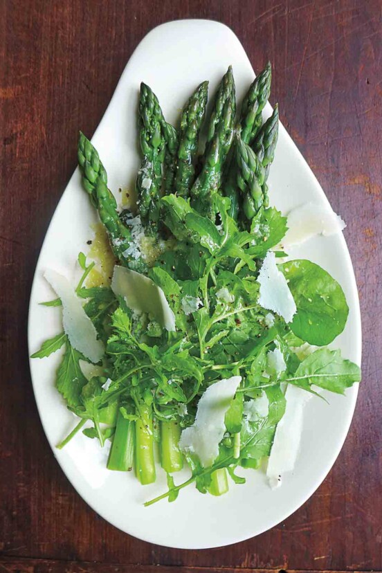 An asparagus and arugula salad topped with Parmesan on a teardrop-shaped plate.