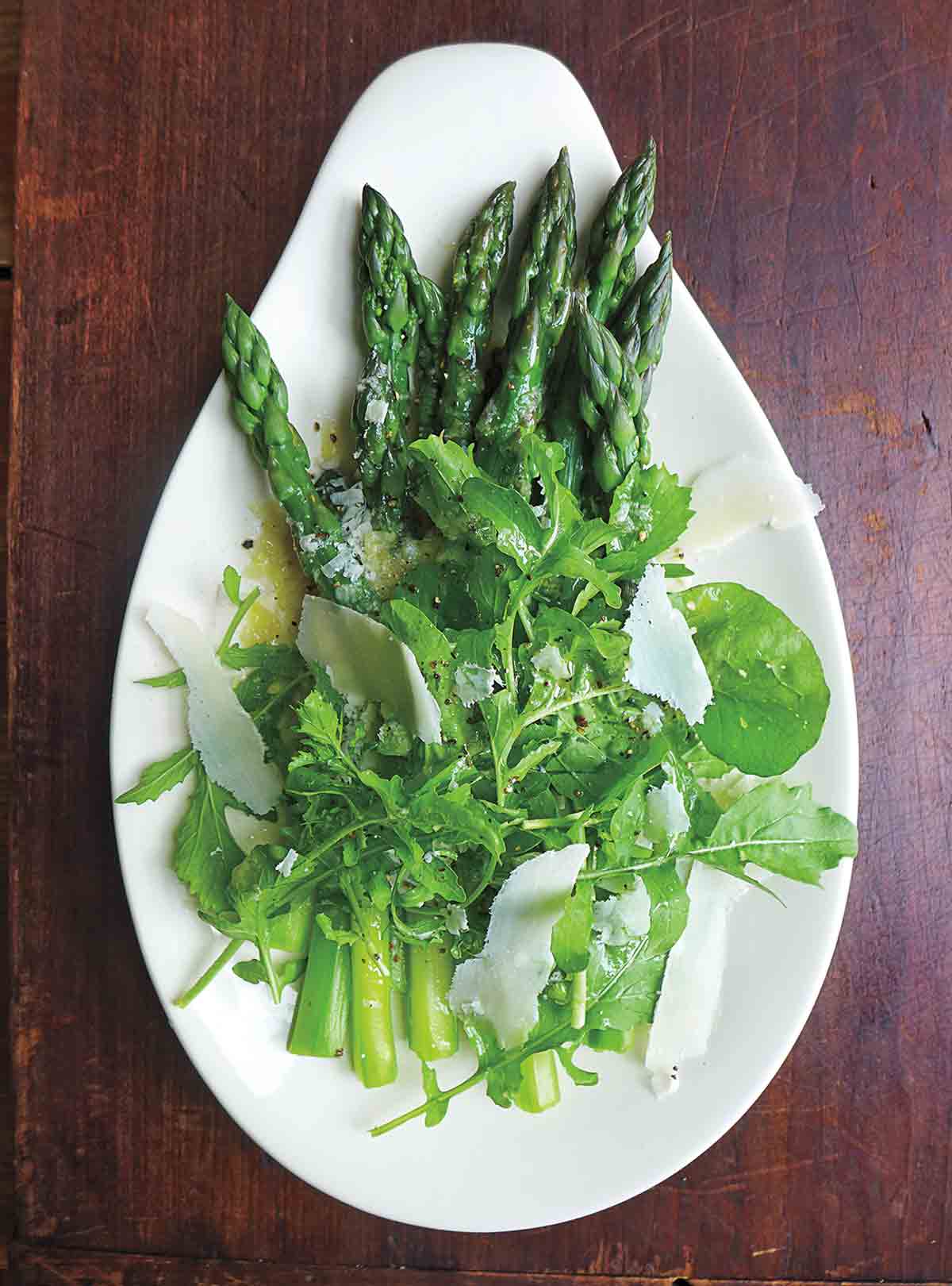 An asparagus and arugula salad topped with Parmesan on a teardrop-shaped plate.