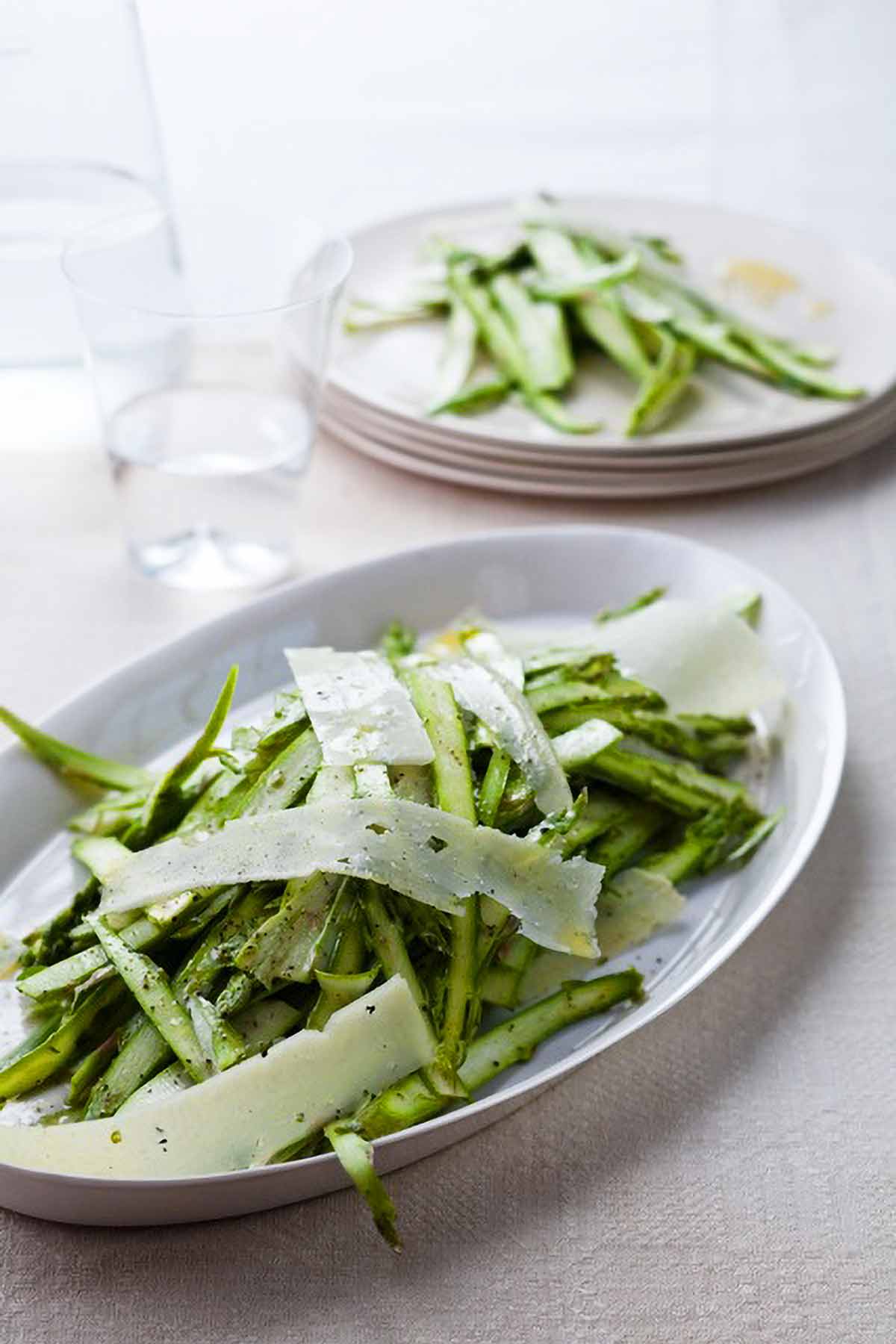 Two plates of shaved asparagus and pecorino salad on a tablecloth.