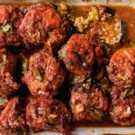 A ceramic baking dish filled with baked kofta -- meatballs on top of eggplant slices, all covered in tomato sauce.