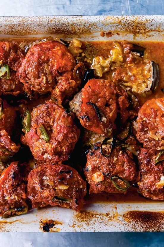 A ceramic baking dish filled with baked kofta -- meatballs on top of eggplant slices, all covered in tomato sauce.