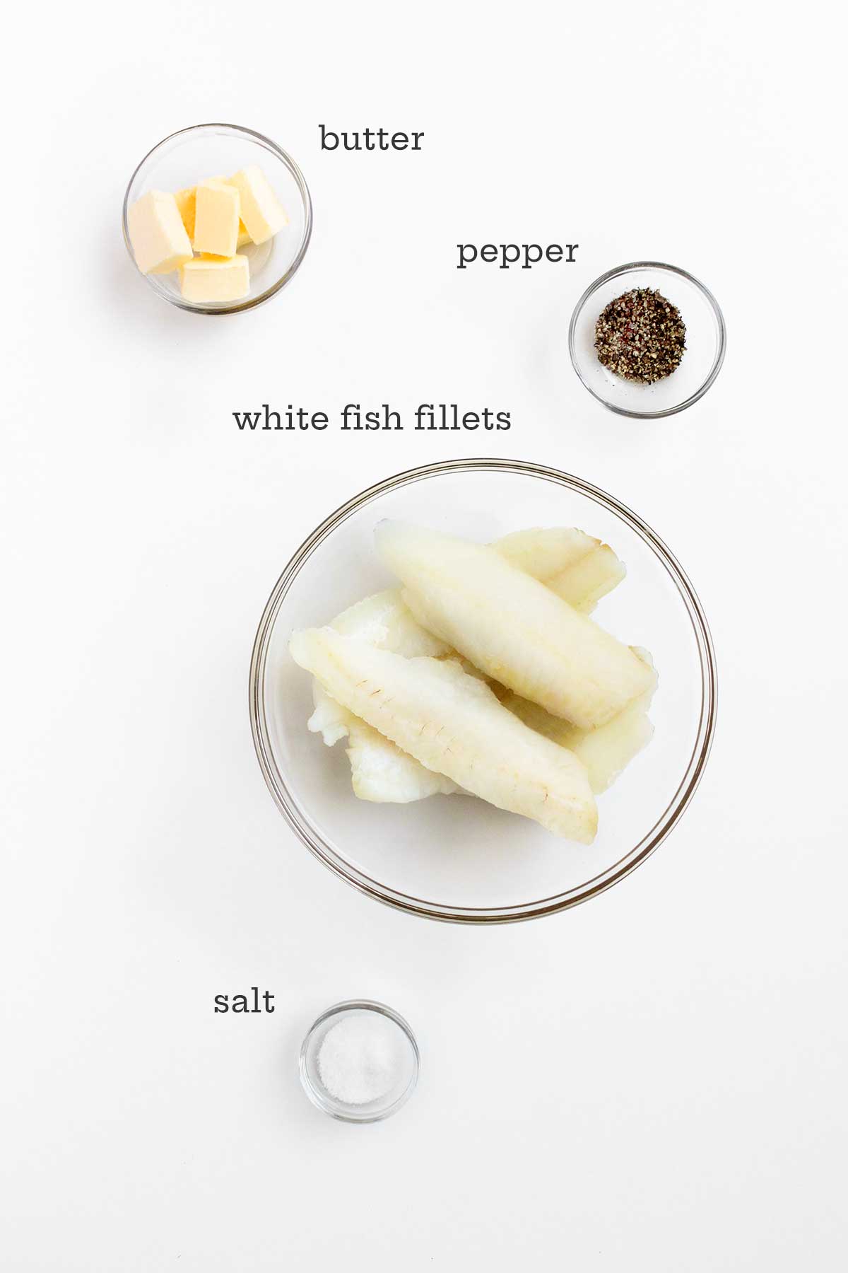 The ingredients for butter baked fish in glass bowls -- butter, pepper, fish fillets, and salt.