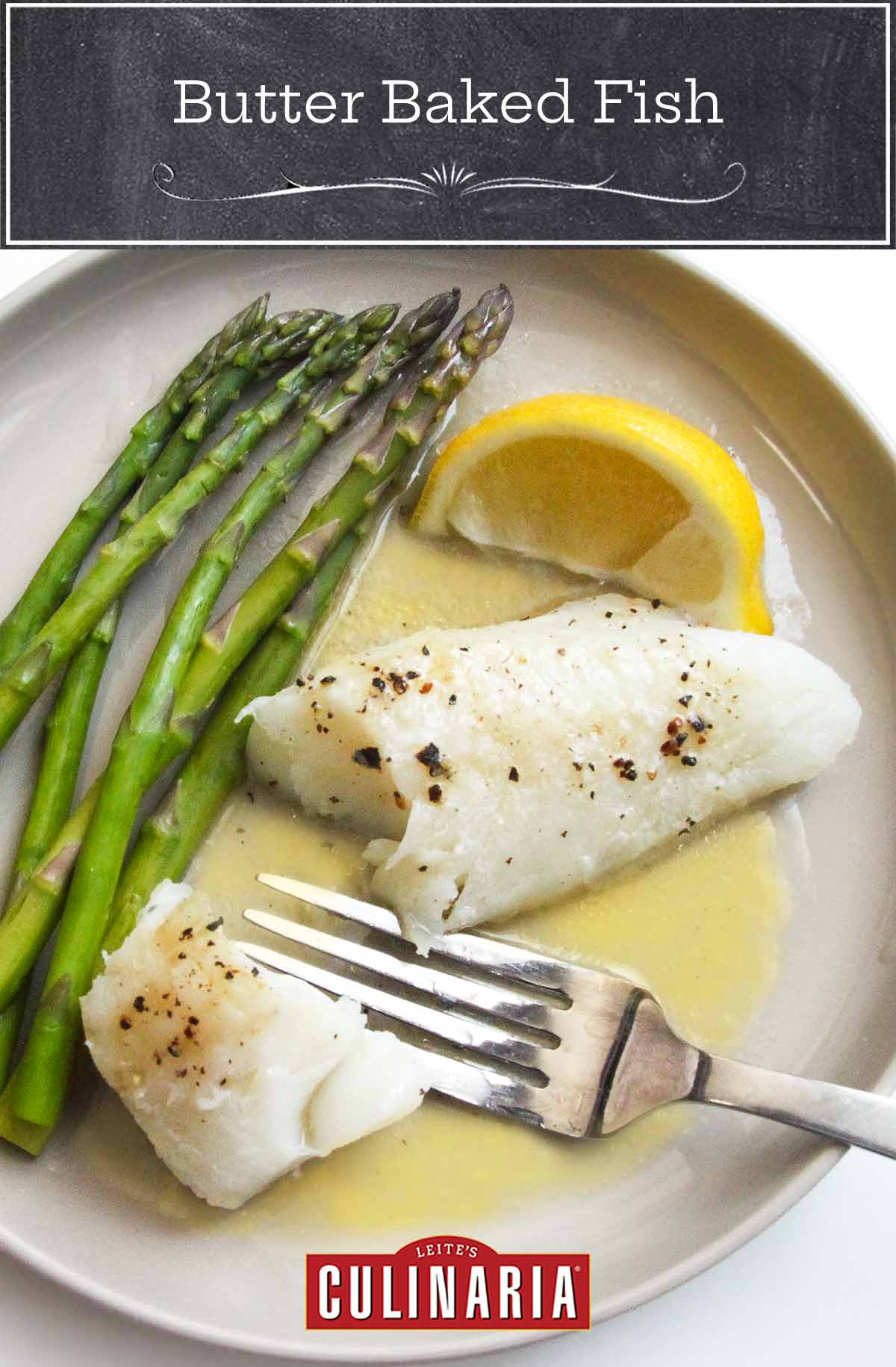 A piece of baked fish on a plate with butter sauce, a lemon wedge, and some asparagus spears.