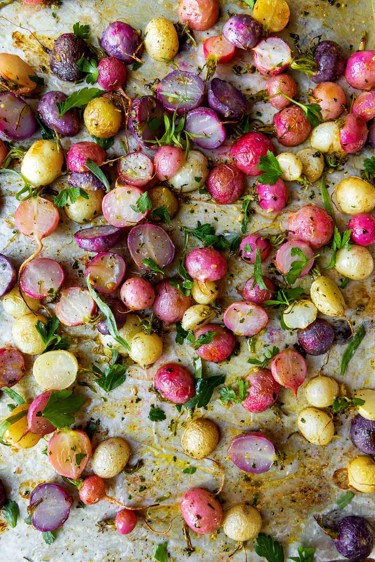 Oven roasted radishes topped with herbs on a baking sheet.