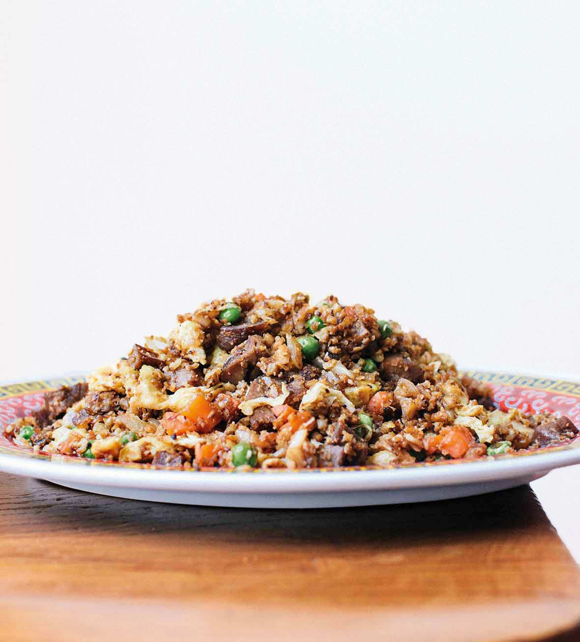 A plate mounded with cauliflower fried rice on a wooden table.