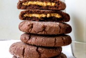 Chocolate peanut butter cookies in a stack, the top one broken in half, on a worn white background.